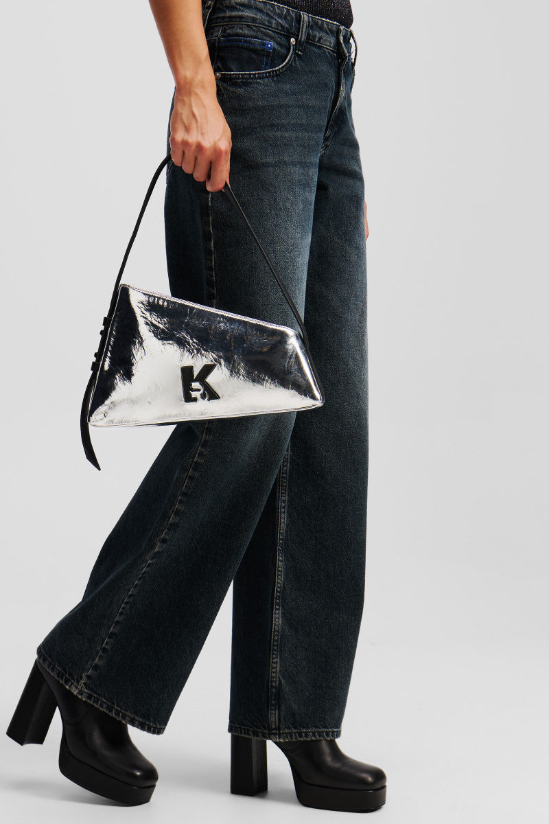 Pochette triangulaire Karl Lagerfeld Jeans argentée métallисée avec logo K noir, portée à la main