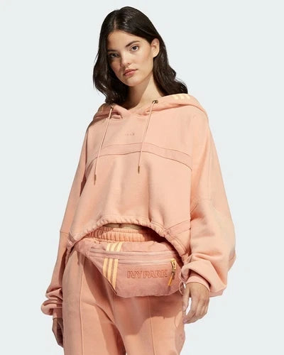 Ensemble Adidas x IVY PARK rose saumon : crop hoodie, jogging et sac banane, porté par une femme